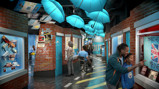 Museum exhibit featuring Manchester City football club items, blue umbrellas, posters, and visitors with children.