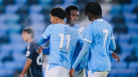 Football players wearing light blue jerseys with numbers 11 and 7, on a football field with blurred background.