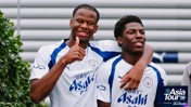 Two Manchester City players in a white and blue jersey smile and pose for a photo, one giving a thumbs-up. 'Asia Tour '26 presented by Abu Dhabi' is visible on the bottom right.