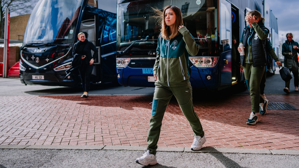 People in green tracksuits arriving at a stadium, with buses in the background.
