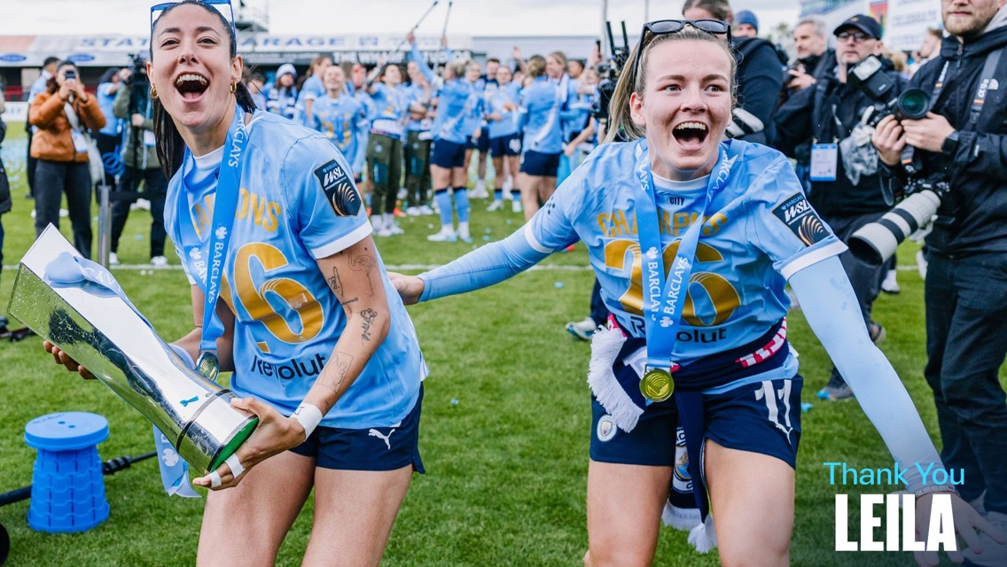 Soccer players in light blue jerseys celebrating on a field, holding a trophy. Text on image indicates a thanks to someone named Leila.