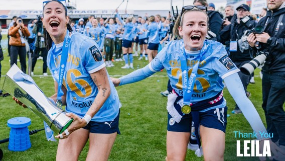 Soccer players in light blue jerseys celebrating on a field, holding a trophy. Text on image indicates a thanks to someone named Leila.