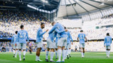 Manchester City players in light blue uniforms celebrating a goal at the Etihad Stadium.