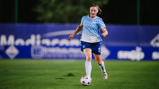 A female soccer player in a Manchester City uniform running with the ball on a field.