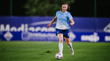 A female soccer player in a Manchester City uniform running with the ball on a field.
