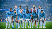Manchester City football team posing for a group photo in blue jerseys at a stadium.