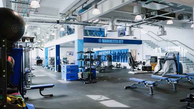 Manchester City gym facility with workout equipment, medicine balls, benches, and blue accents.