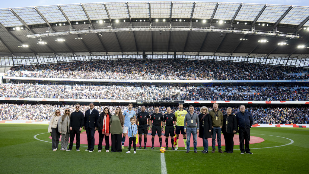 Group posing on the field at Etihad Stadium, with a large crowd in the stands.
