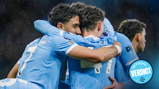 Manchester City players in blue jerseys embrace in a goal celebration during a Premier League match. The image features the official verdict logo.