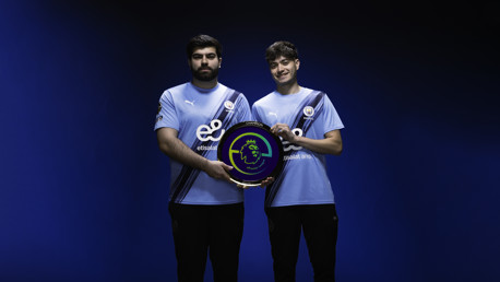 Two people in Manchester City esports jerseys holding an ePremier League champion trophy.