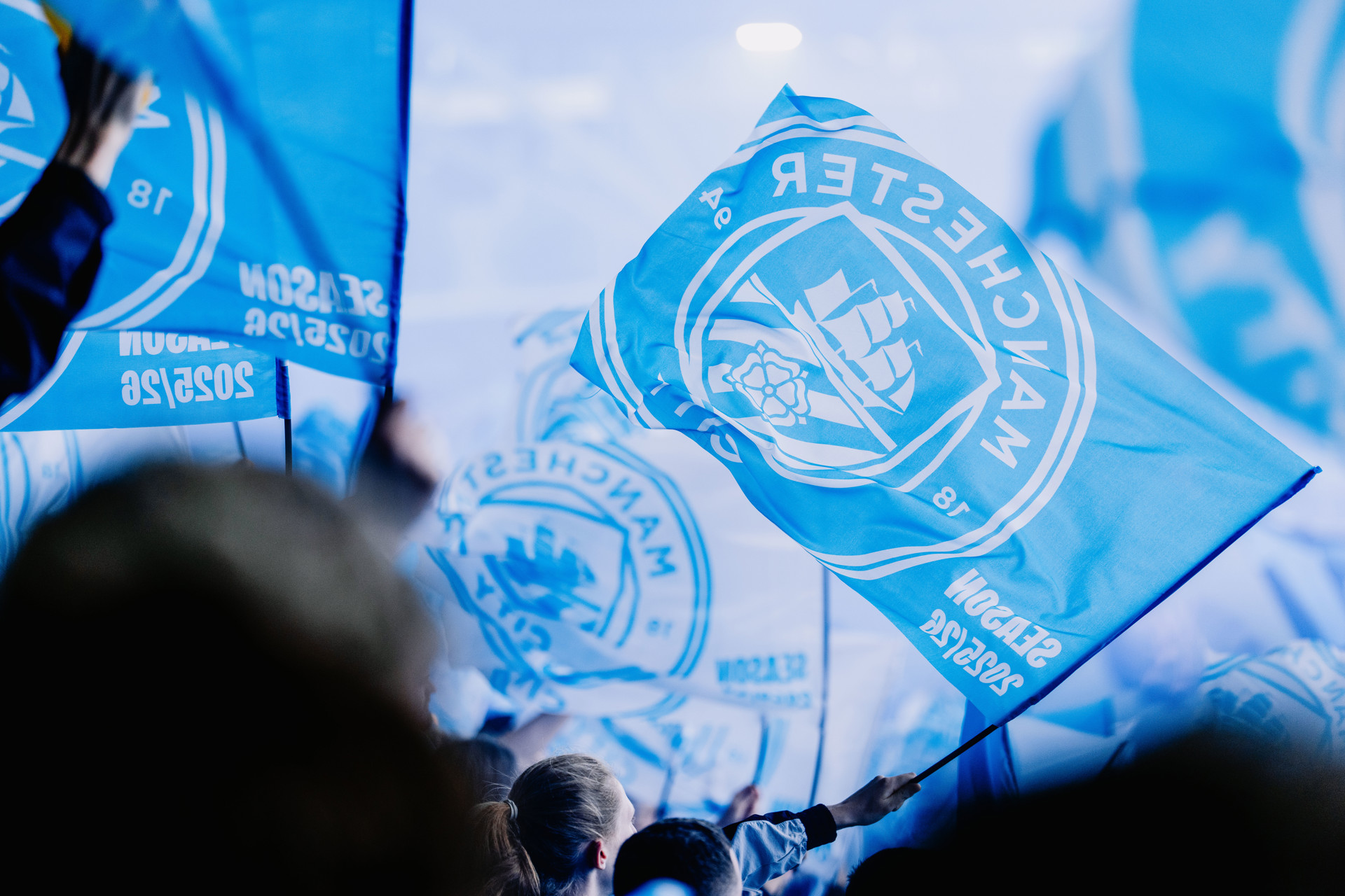 Blue flags with the Manchester City logo being waved by a crowd of supporters.