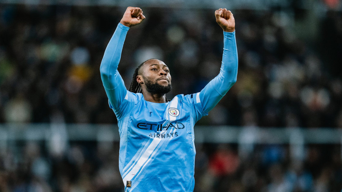 A Manchester City player wearing the team's blue jersey with arms raised in celebration. The jersey features the club crest and sponsorship logo.