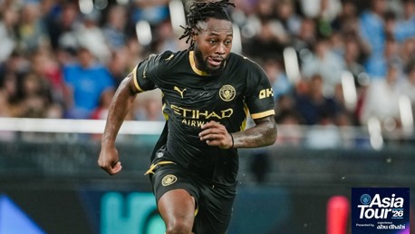 A Manchester City player in a black kit running during the Asia Tour '26 in a stadium.