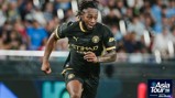 A Manchester City player in a black kit running during the Asia Tour '26 in a stadium.