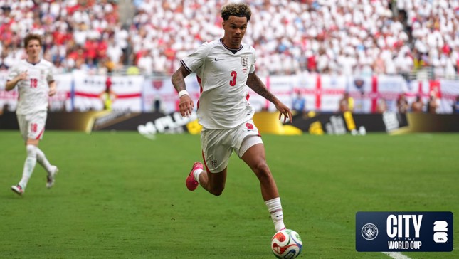Soccer player wearing a white jersey with the number 3 on it running with the ball on the field during a World Cup match. The crowd is visible in the background with England flags and a logo for City at the World Cup in the corner.