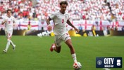 Soccer player wearing a white jersey with the number 3 on it running with the ball on the field during a World Cup match. The crowd is visible in the background with England flags and a logo for City at the World Cup in the corner.