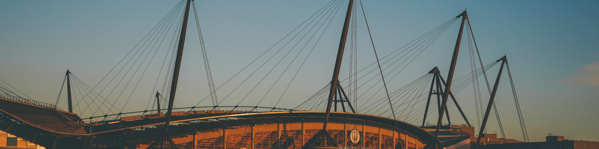 The Etihad Stadium illuminated during sunset, featuring its iconic spirals and Manchester City branding.