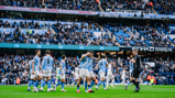 Manchester City players celebrating a goal at Etihad Stadium with a crowded audience in the background.