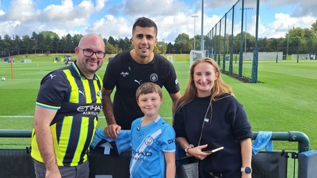 A family poses with a Manchester City player wearing team gear at a training facility.