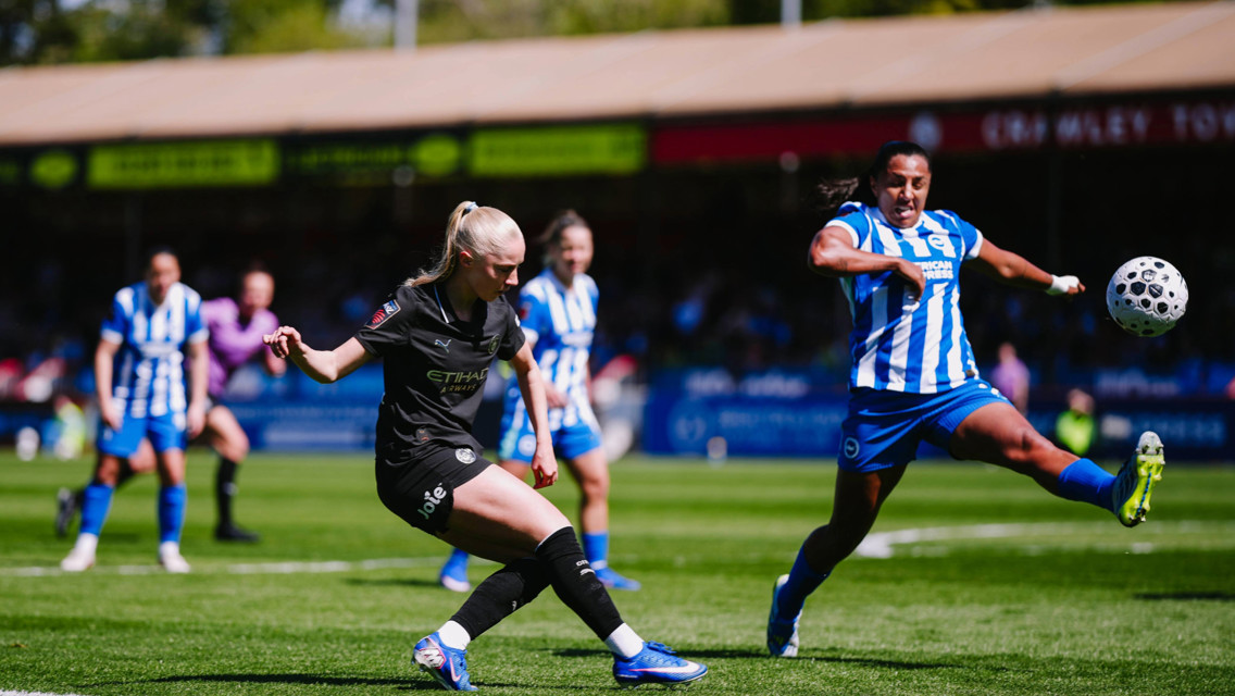 A soccer match scene with players from two teams, one in black jerseys and the other in blue and white stripes, vying for possession of the ball.