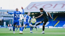 Soccer match at Kenilworth Road with players from opposing teams in action. Players are sporting blue and white kit versus black kit.