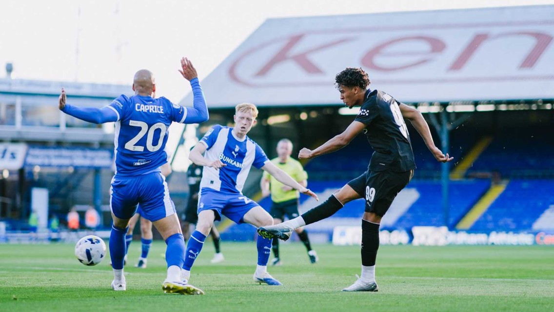 Soccer match at Kenilworth Road with players from opposing teams in action. Players are sporting blue and white kit versus black kit.