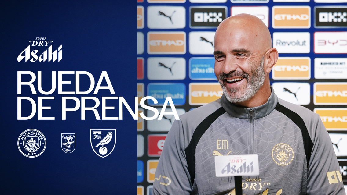 Smiling man with Manchester City attire during a press conference with Asahi branding in the background.
