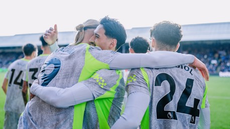 Manchester City players celebrate a goal wearing grey and neon green kits with visible Premier League logos on their backs. Numbers and names include Akanji (9), Laporte (14), and Gvardiol (24).