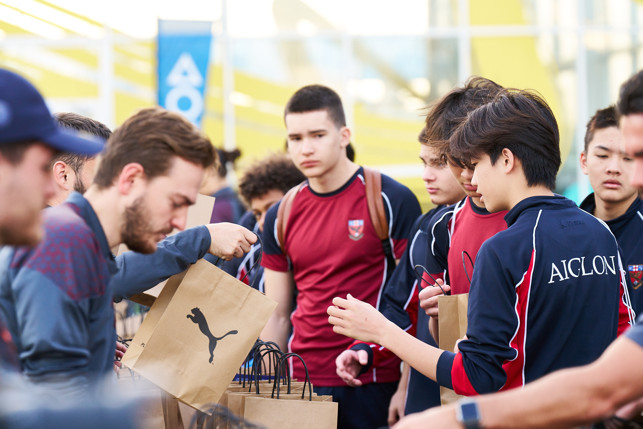 Several students, wearing school uniforms with Aiglon branding, are participating in a school event where they are receiving Puma gift bags. The background includes a banner with the text 'A O'.