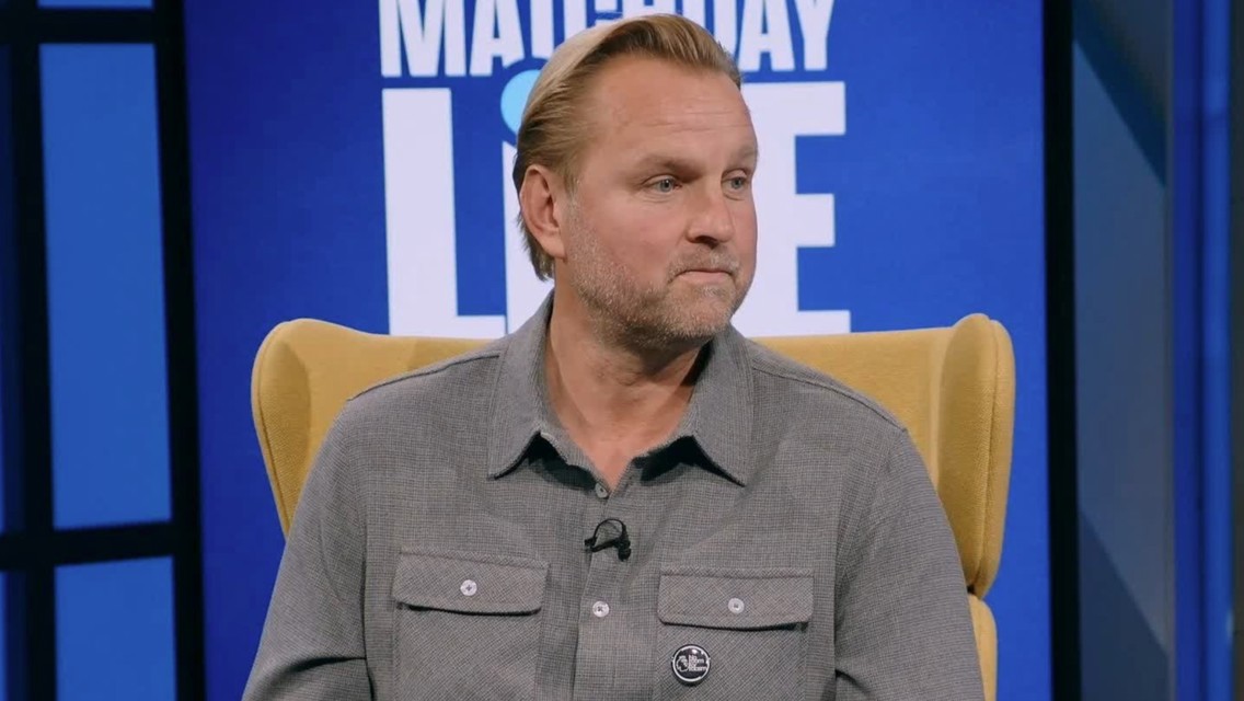 A man with a light beard and short hair wearing a grey shirt sits on a yellow chair. The background features the text 'Matchday Live'.