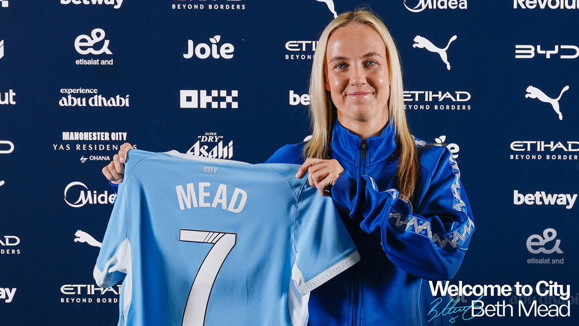 A person holding a Manchester City jersey with the name 'Mead' and the number 7 at a welcome event.