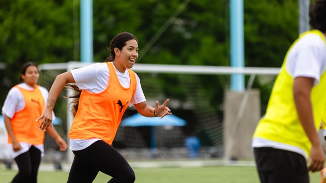 Women wearing orange and yellow vests participating in soccer training on a field.