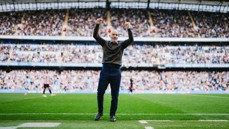 A person standing on a soccer field with their arms raised in celebration, surrounded by a full stadium crowd.