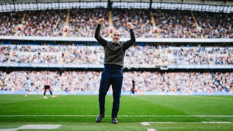 A person standing on a soccer field with their arms raised in celebration, surrounded by a full stadium crowd.