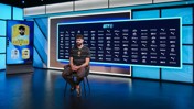 A person in a Manchester City jersey sits at a press conference, with a digital display showing club sponsors and graphics including player cards featuring 'Gvardiol'.