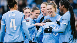 Manchester City women's soccer team in a huddle wearing light blue uniforms with the players' names 'ROSE' and 'AUBA' visible.