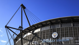 View of Etihad Stadium with Manchester City logo and clear blue sky.