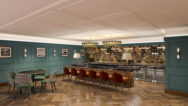 A stylish bar interior featuring teal walls, wooden herringbone flooring, orange bar stools, and a dark marble countertop. Decor includes framed photographs and patterned chairs around a round table.
