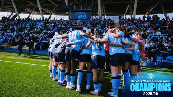 Manchester City Women's team celebrates as they win the Barclays Women's Super League 2025/26, with players huddled on the pitch in front of cheering spectators.