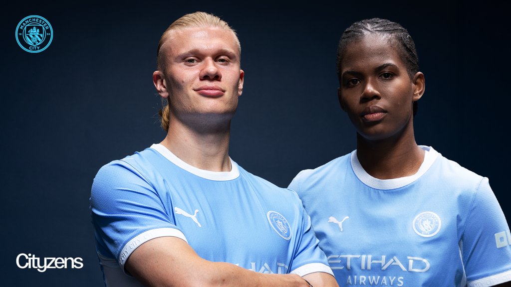 Two Manchester City players in the 2026/27 home kit, standing confidently with club logos in the background.