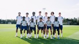 A group photo of eleven young soccer players in Manchester City training kits on a grassy field.