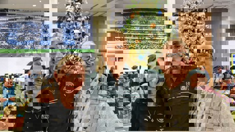 Three people standing near a decorated Christmas tree at a Manchester City gathering.