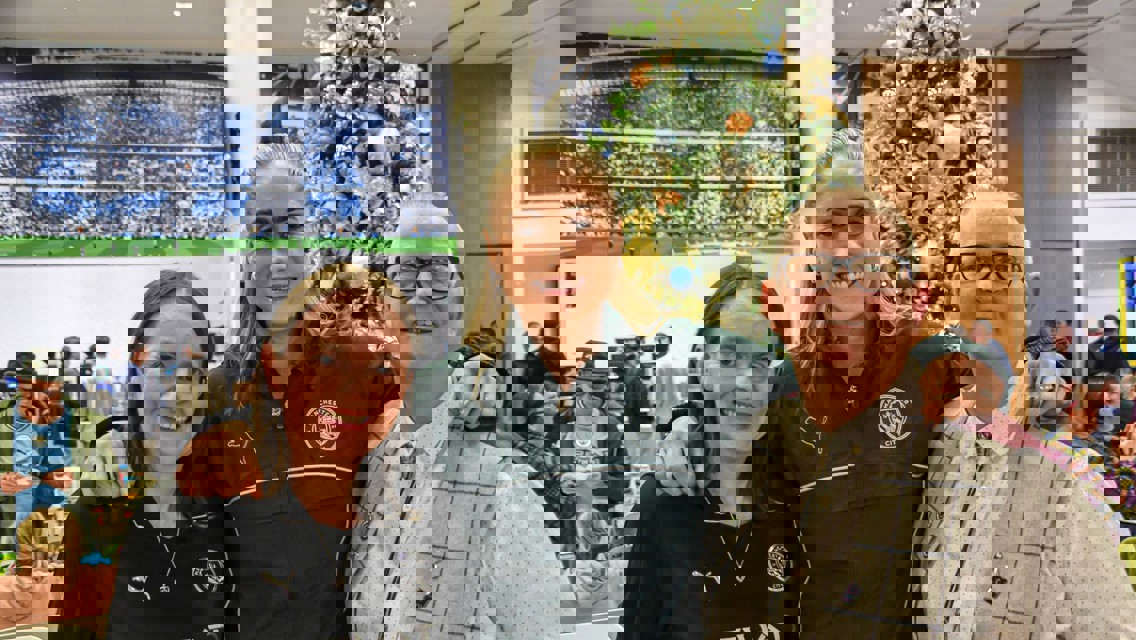 Three people standing near a decorated Christmas tree at a Manchester City gathering.