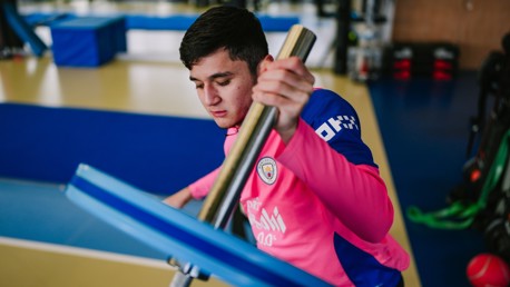 A person wearing a pink Manchester City jersey is training in a gym, handling gym equipment.