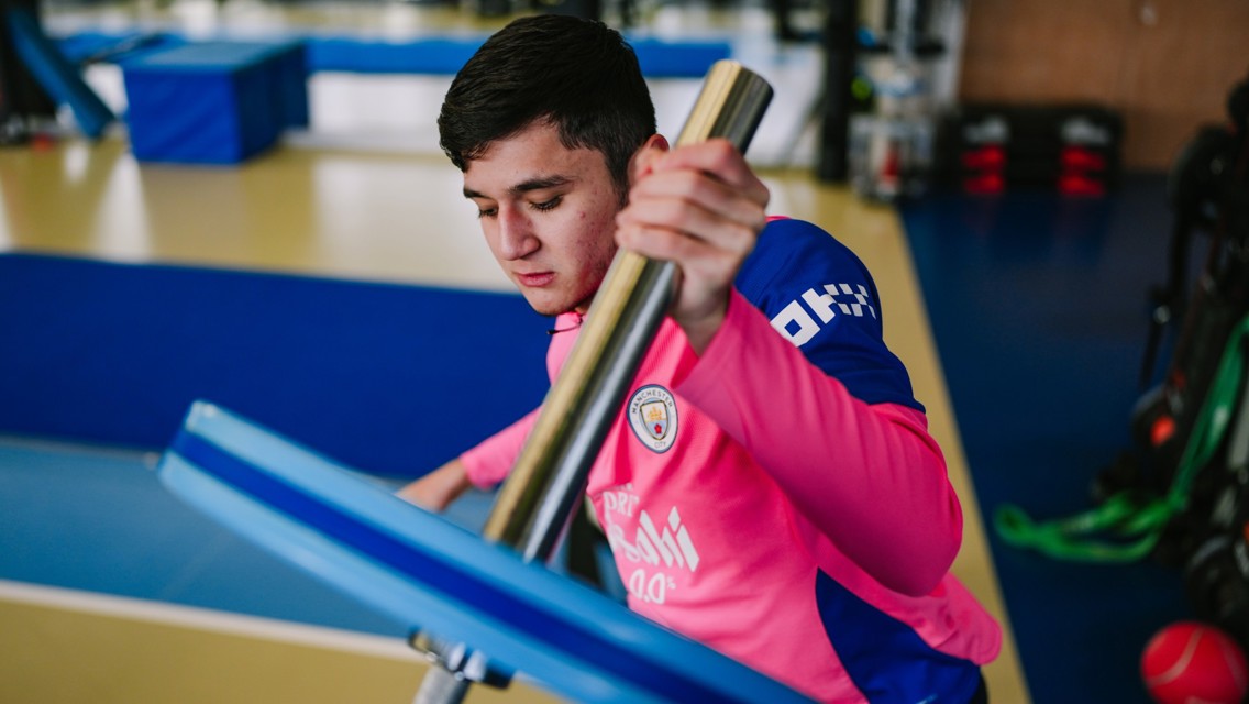 A person wearing a pink Manchester City jersey is training in a gym, handling gym equipment.