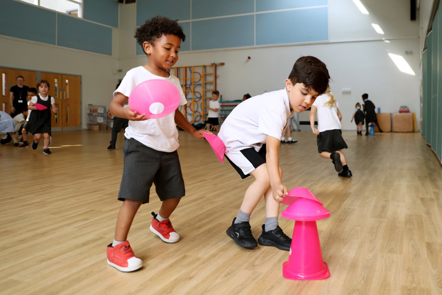 Children playing with pink cones in a gym. They appear to be engaged in a physical activity session.