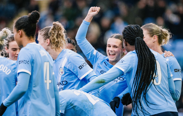 A group of Manchester City women's soccer players celebrating on the field in light blue jerseys.