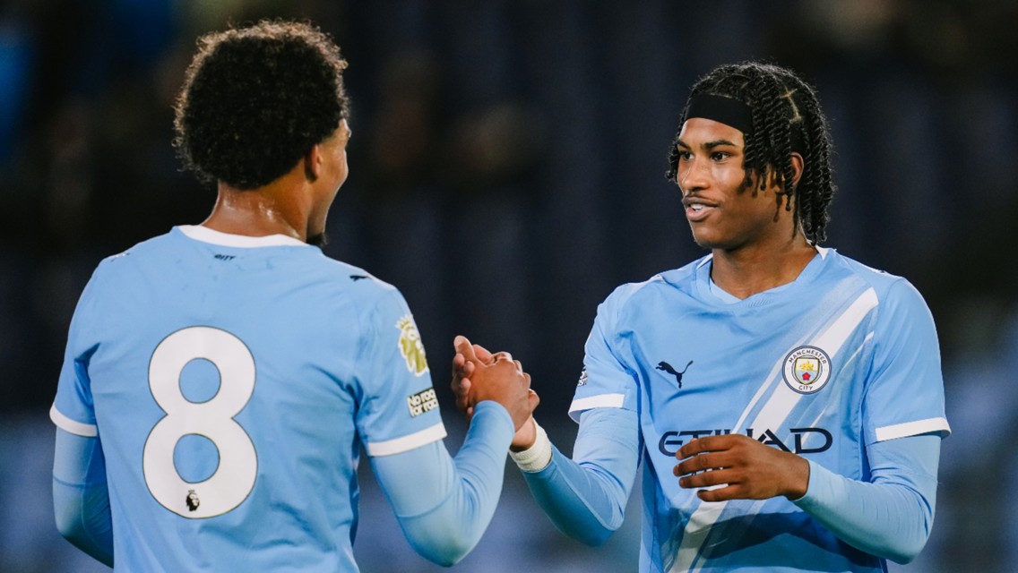 Two Manchester City players shaking hands wearing blue jerseys with the number 8 visible. One jersey features Manchester City logos.