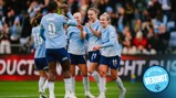 Manchester City women's football team celebrates a goal on the field. Players in light blue jerseys are cheering and clapping.