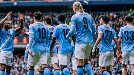 Manchester City football players in team kit celebrating on the field, featuring player numbers and names on their backs.